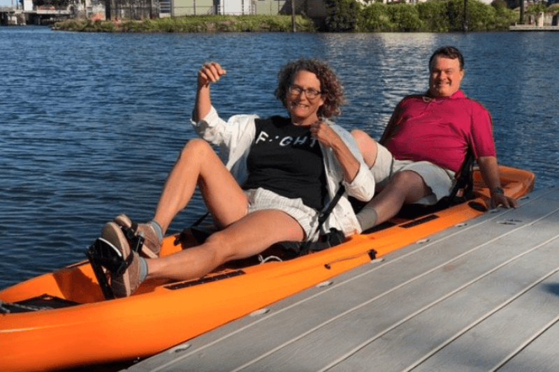 Smiling man and woman in pedal-powered kayak at a dock. 