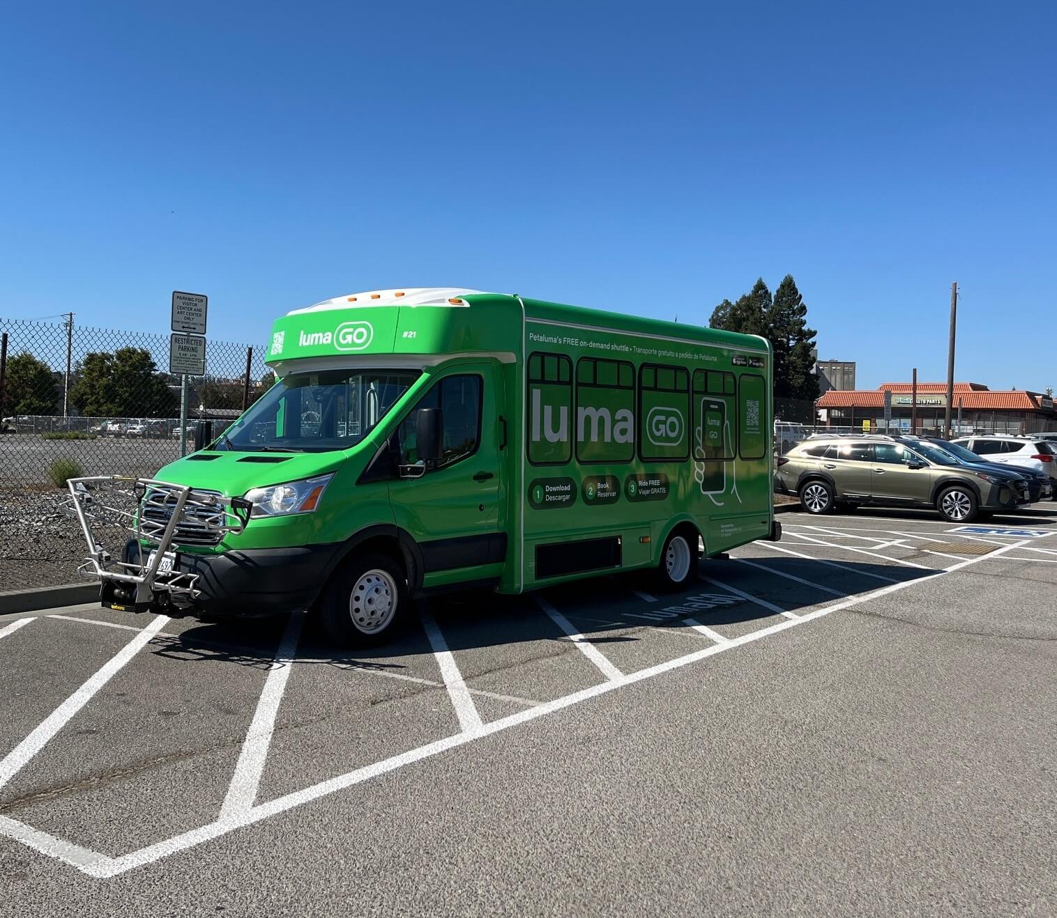 Green LumaGo shuttle in parking lot under blue skies.