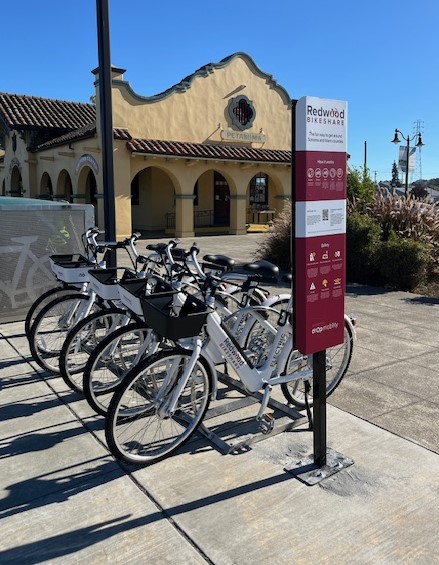 White electric bikes in bike rack with Petaluma Train Depot in background