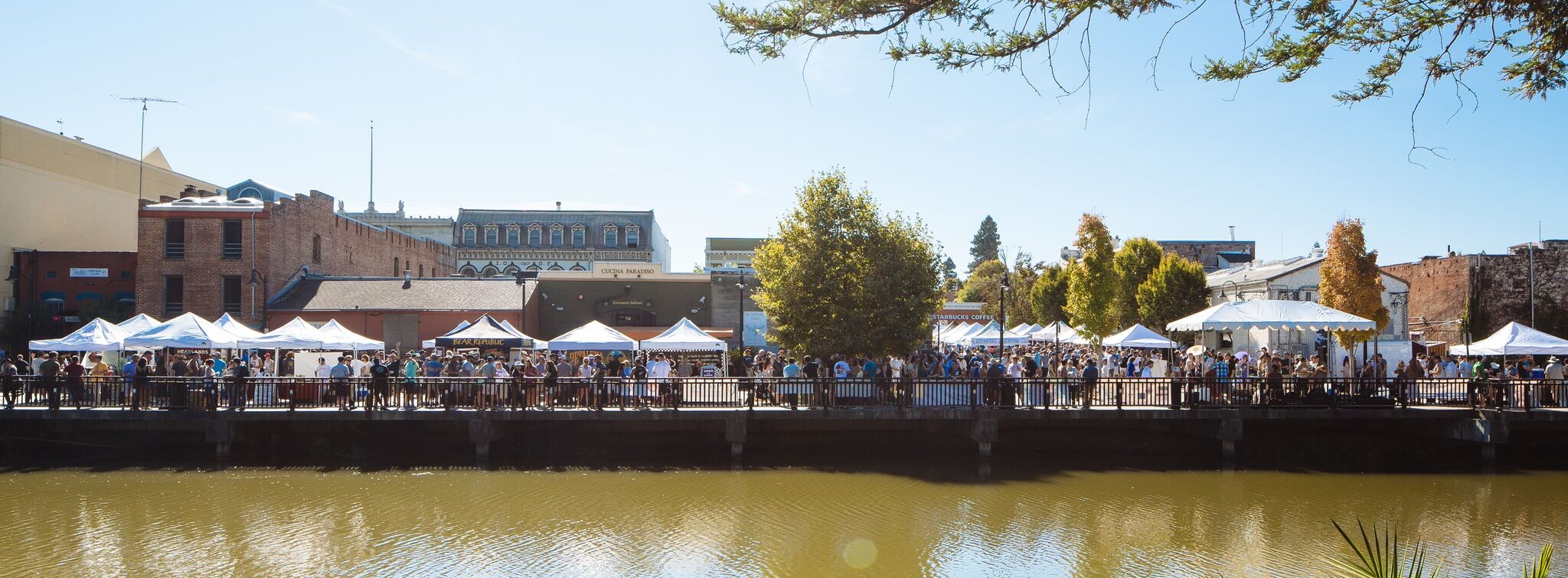 Street fair along  a riverfront road as seen from across the river