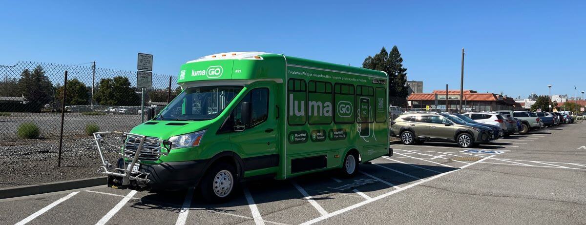 Green LumaGo shuttle, with bike racks on front, parked in parking lot's designated area.