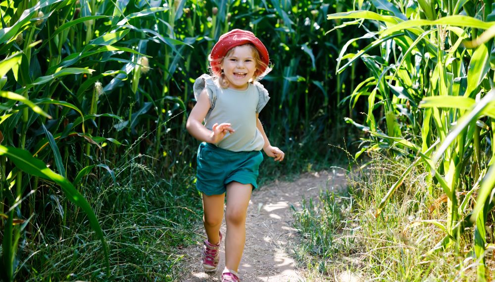 girl in shorts and red hat running through corn maze