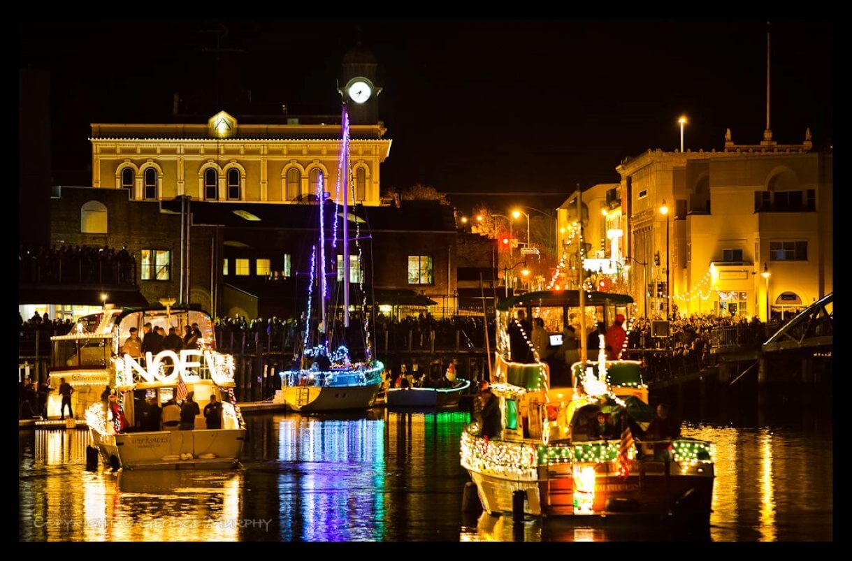 Night on a river with boats decked out in holiday lights with reflections off the water - Copyright George Murphy