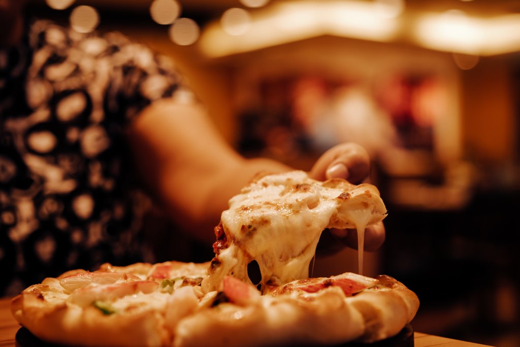 Woman's hand lifting a very cheesy slice of pizza from a full deep-dish pie. 